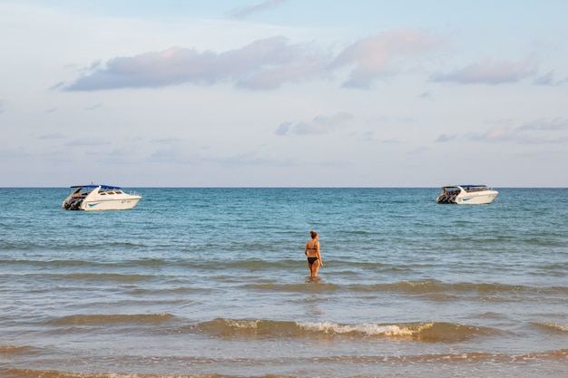 Back of a woman wearing bikini standing in the sea with speed boats.