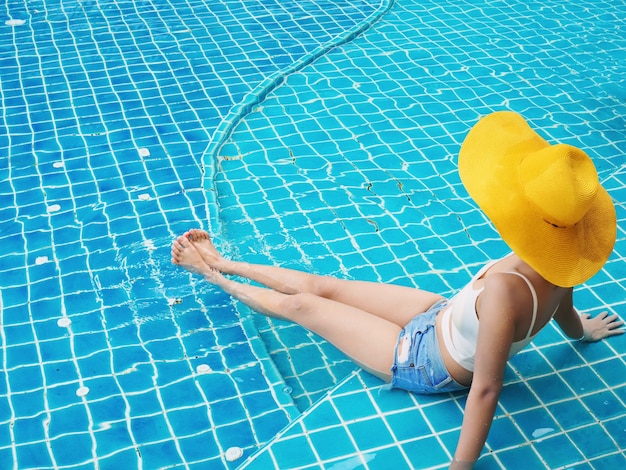 Back of woman with yellow hat sitting on swimming pool