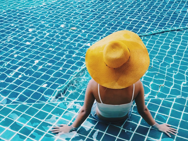 Back of woman with yellow hat sitting on swimming pool