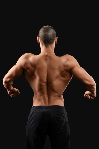 Back work. Male bodybuilder showing off his toned muscular back posing on dark