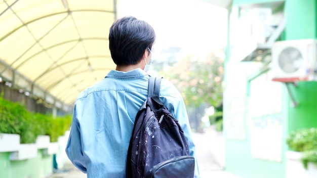 Back of young asian campus student man wearing protection mask while walking in campus