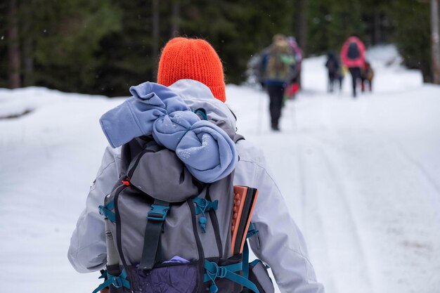 The back of a young hiker with a white ski costume and a bright colorful hat Winter season