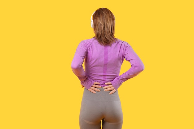 The back of a young woman with backaches in a studio over yellow background