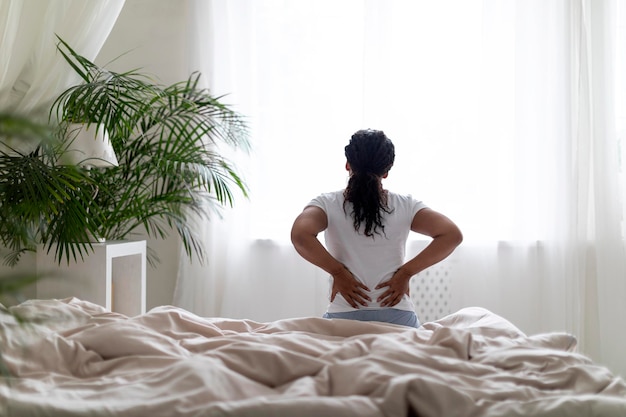 backache concept young black woman massaging aching back while sitting in bed