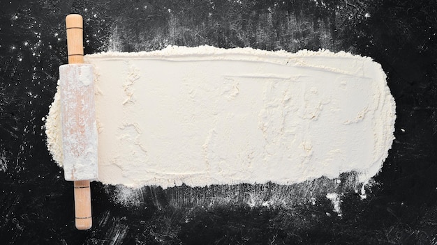 The background of baking rolling pin and flour on a black background Top view Free copy space