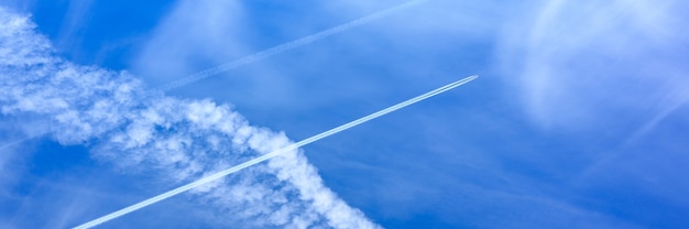 白い雲と飛行機からのトレイルと美しい明るい青い日の空の背景。バナー