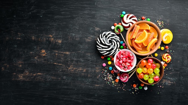 Background of colored candies and lollipops Sweets On a black background Top view free copying space