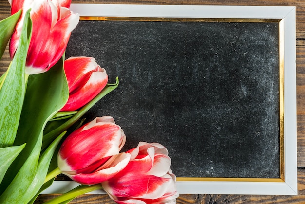 Background for congratulations greeting cards fresh spring tulips flowers with chalkboard for text on a wooden background