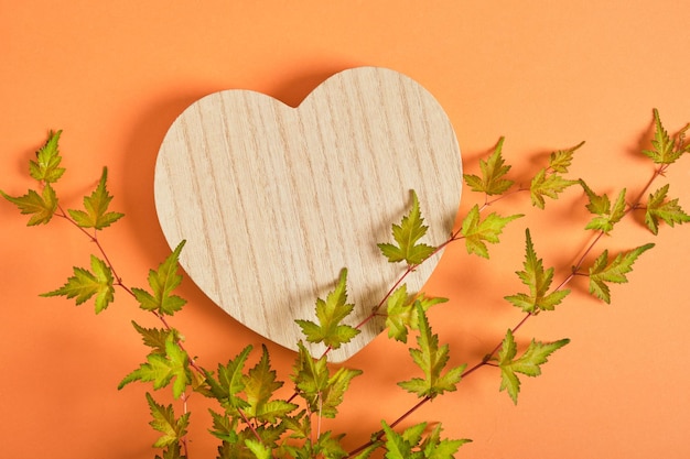 Background for cosmetic products wooden heart podium with green leaves topview