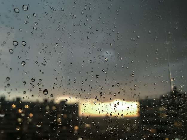 水滴の背景。窓ガラスの雨滴。雨滴の自然なパターン。ガラスに雨滴の抽象的なショット。夜の街と窓の外の夕日。セレクティブフォーカス。テキストまたはロゴ用のスペース