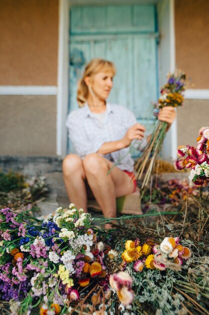 背景女性の花屋は、花に焦点を当てたドライフラワーの美しい構図を作成します垂直