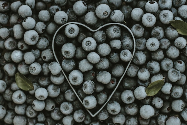 Background of fresh frozen blueberries with a metal heart shape. Texture of blueberries close-up. the summer harvest of berries. space for text