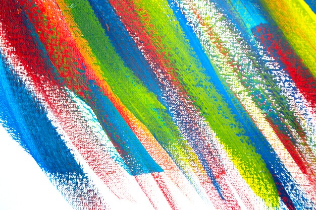 Background from different strokes of red, yellow, green and blue paint with brush on white background close-up. Bright colorful backdrop of brush lines. Mixing color streaks of paint on white canvas