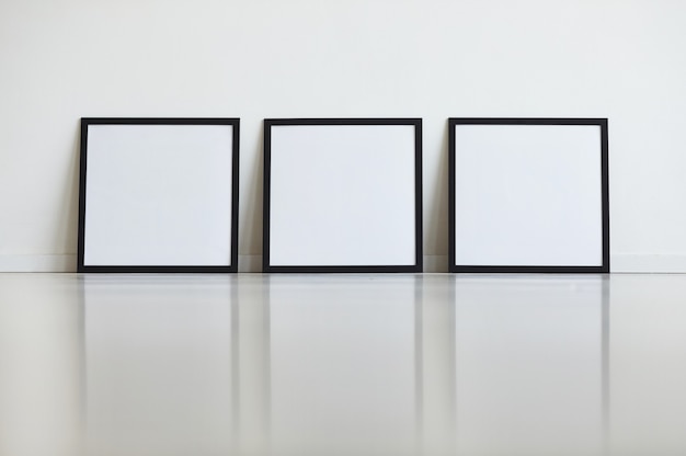 アートギャラリーの白い壁に並んで設定された3つの同一の黒いフレームの背景画像、