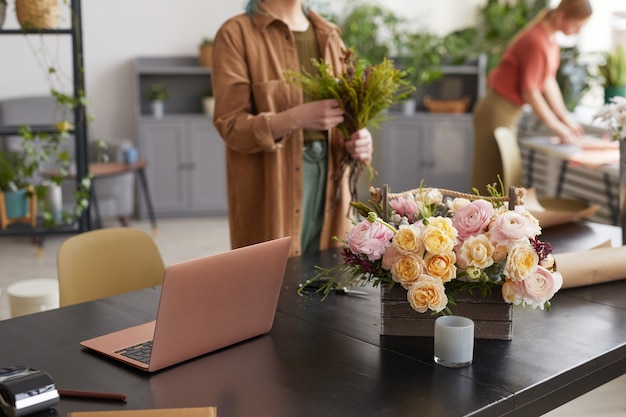 Photo background image of open laptop on table in flower shop with unrecognizable female florist in background, copy space