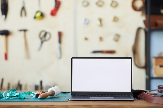 Background image of open laptop with blank white screen on table in tanners workshop small business ...