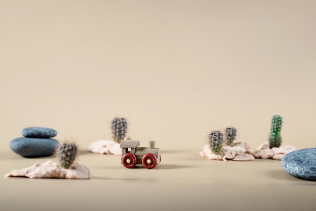 Photo background image of wooden toy steam locomotive in desert with stones and cactuses on beige backdrop