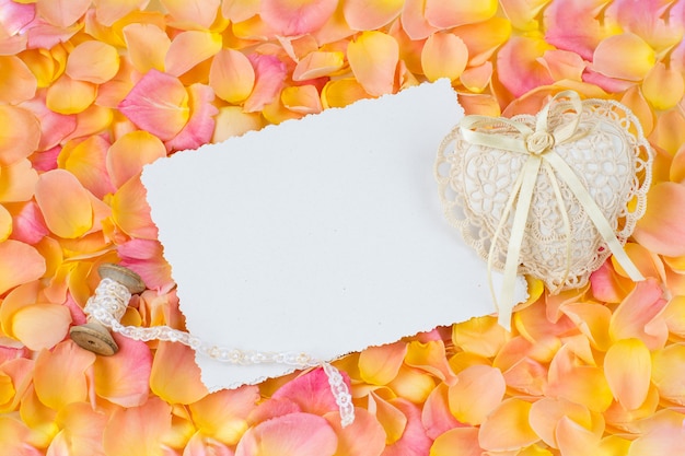 background of pink rose petals, paper sheet, heart of lace and ribbon 