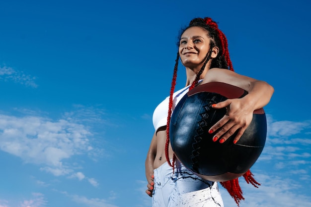 背景の空 メッドボールを持ったアスレチックな女性 強さとモチベーションファッショナブルなスポーツウェアを着たスポーティーな女性の写真