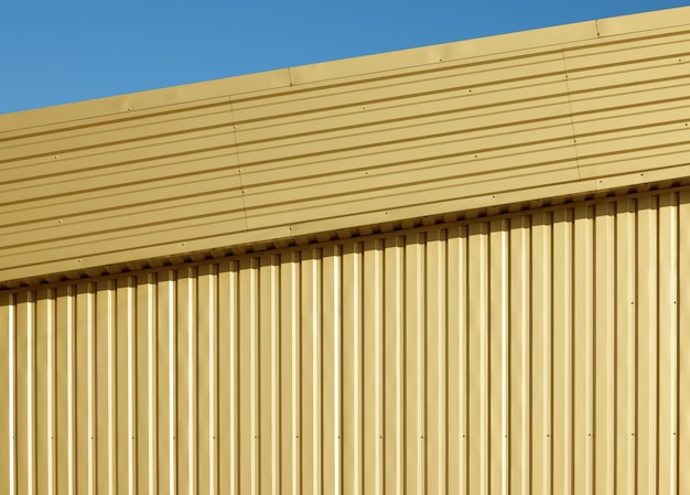 青空の下で金色のアルミニウムの波形のgoffered金属壁の背景のテクスチャ
