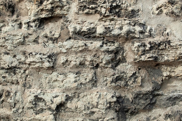 Background uneven concrete wall in holes gray and protruding stones For decoration