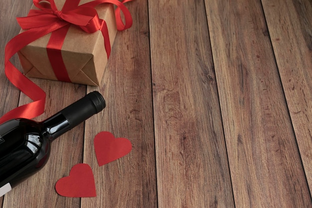 Sfondo per san valentino una bottiglia di vino un regalo di carta kraft un cuore e un nastro rosso satinato su uno sfondo di legno