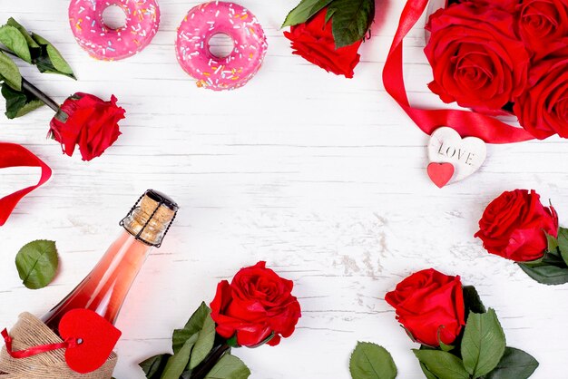 background for Valentines day with a bottle of champagne heart red roses donuts on a wooden