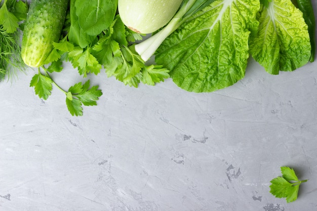 Sfondo con verdure verdi, insalata, cetriolo, cipolla verde e zucchine sul tavolo di pietra grigia. concetto di cibo sano con spazio di copia.