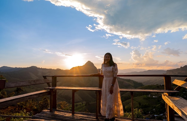 backlight happy Asian woman standing at wooden terrace with beautiful sunset mountain view at Huai Hia viewpoint, Pang Mapha, Mae Hong Son, Thailand