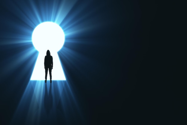 Подсветленный человек в капюшоне, стоящий в ярком замочном отверстии, открывающемся на темном фоне с макетным местом и световыми лучами. Концепция мечты о будущем и возможностях