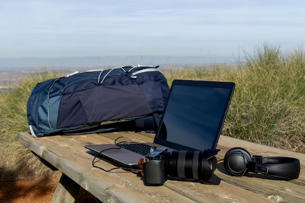 Backpack computer camera and headphones on a table in the wilderness digital nomad concept