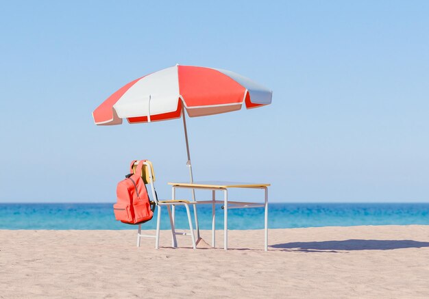 Backpack and Desk Under Beach Umbrella on Sandy Shore