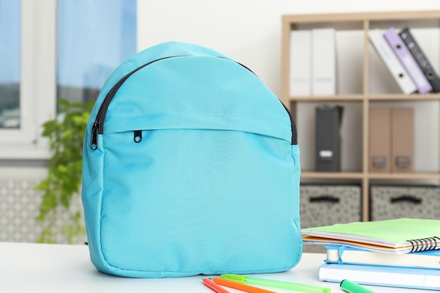 backpack and different school stationery on white table indoors