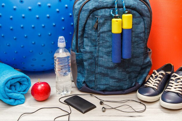 Backpack, mobile phone with headphones and different tools for fitness in room or gym on grey floor