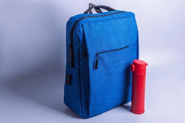 Backpack and a thermos for water stand side by side on a monochrome background