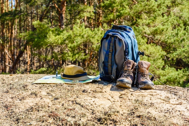 Backpack, touristic boots, map, compass and hat on a ground in a coniferous forest