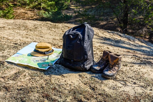 Рюкзак, туристические ботинки, карта, компас и шляпа на земле