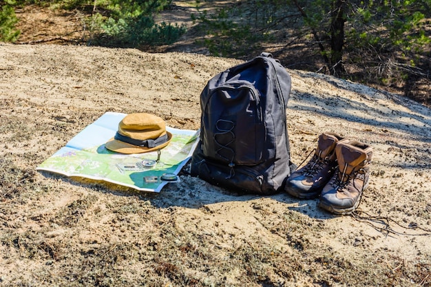 Backpack, touristic boots, map, compass and hat on a ground