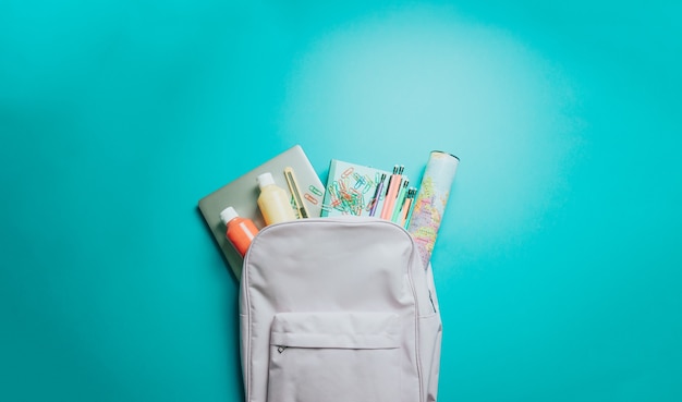 Zaino con materiale scolastico colorato su sfondo viola. di nuovo a scuola. disposizione piatta, vista dall'alto, copia spazio, design minimale