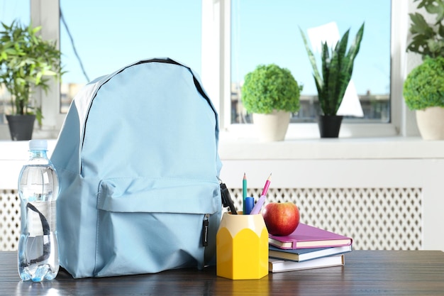 backpack with different school stationery apple and bottle of water on wooden table indoors