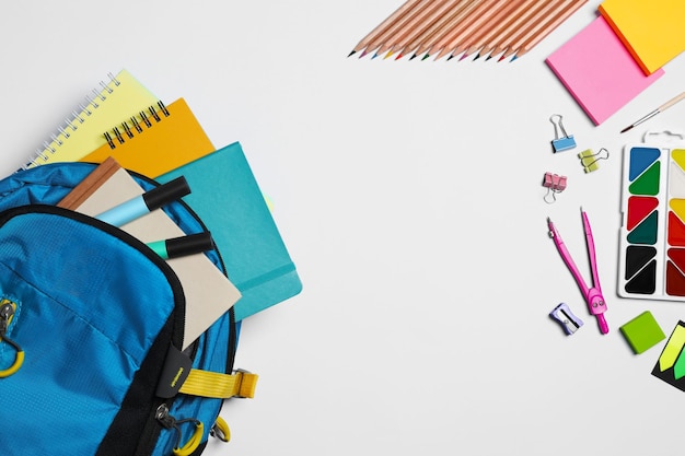 Backpack with different school stationery on white background flat lay Space for text