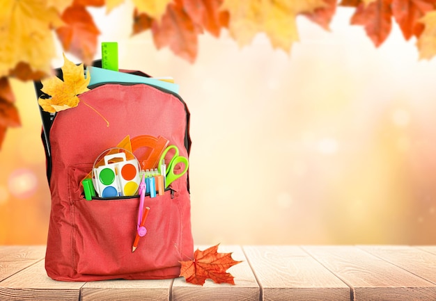 backpack with school supplies on autumn background with falling leaves