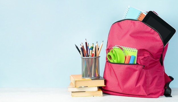 Backpack with school supplies, books and pencil holder on a light blue background