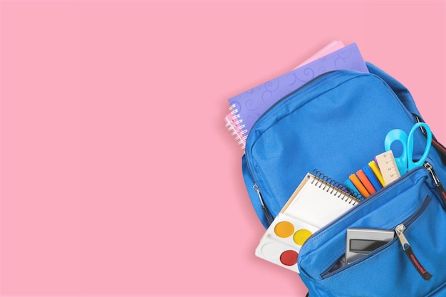 Backpack with school supplies top view on pink empty space background.