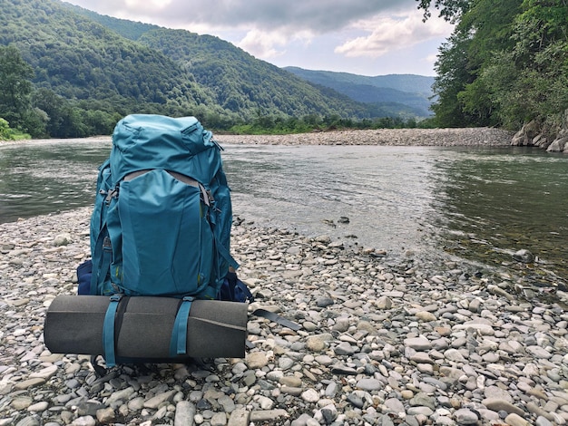 Backpack with tourist mat in campsite at river and mountains background