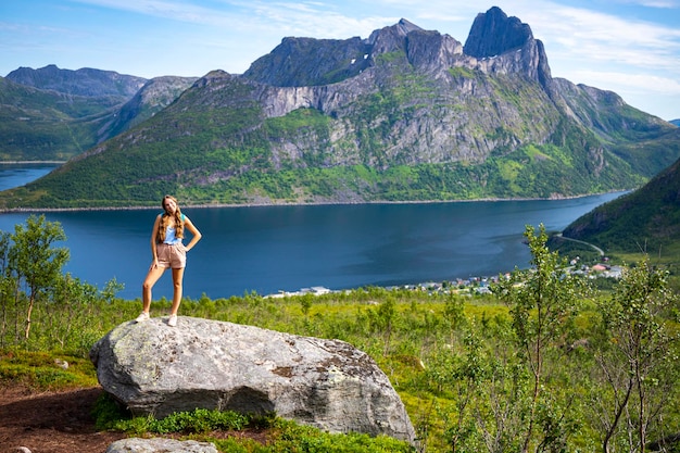 backpacker girl hiking hesten trailhead overlooking town of fjordgard and mighty mountains, senja