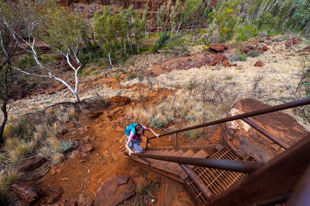 backpacker girl hiking on red rocks up a steep mountain in karijini national park in australia