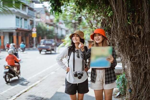 Backpacker girl pointing with a finger at directions while using a map with a friend while searching