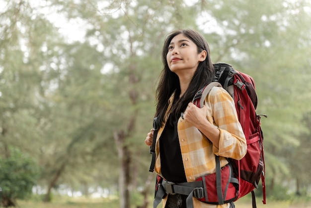 Backpacking and hiking travel concept Asian women look up to the top with a big red bag to explore nature.