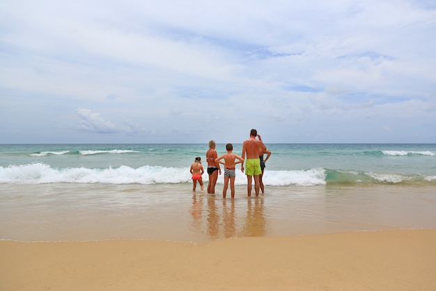 Спины членов семьи, стоящих на песчаном берегу перед морем